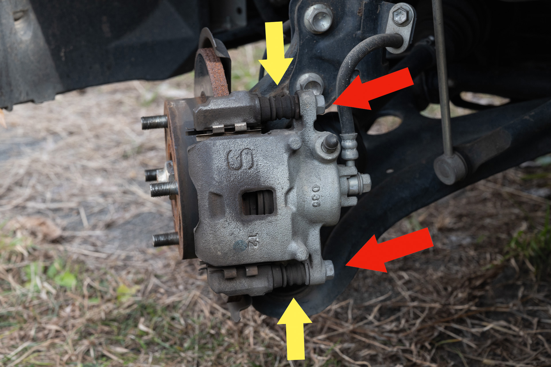 パッドの清掃や交換だけなら下の1本を外せば良い。スライドピンを清掃する場合は赤を2本とも外す。するとキャリパーが落ちるので注意