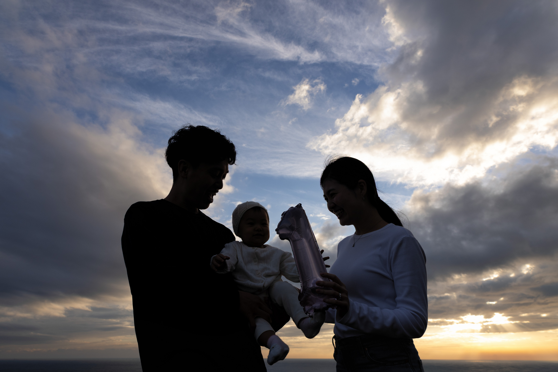 昨年11月誕生の孫娘が1歳になり、息子夫婦に家族写真の撮影を頼まれて近くの海へ。夕暮れ空を背景にほぼ撮って出しで、人物は後から明るく持ち上げるのですが、ここでは画像編集前の状態でチラ見せです<br>EOS R6 Mark II／RF24-105mm F4-7.1 IS STM／24mm／マニュアル露出（1/320秒、F8.0）ISO200／WB：太陽光