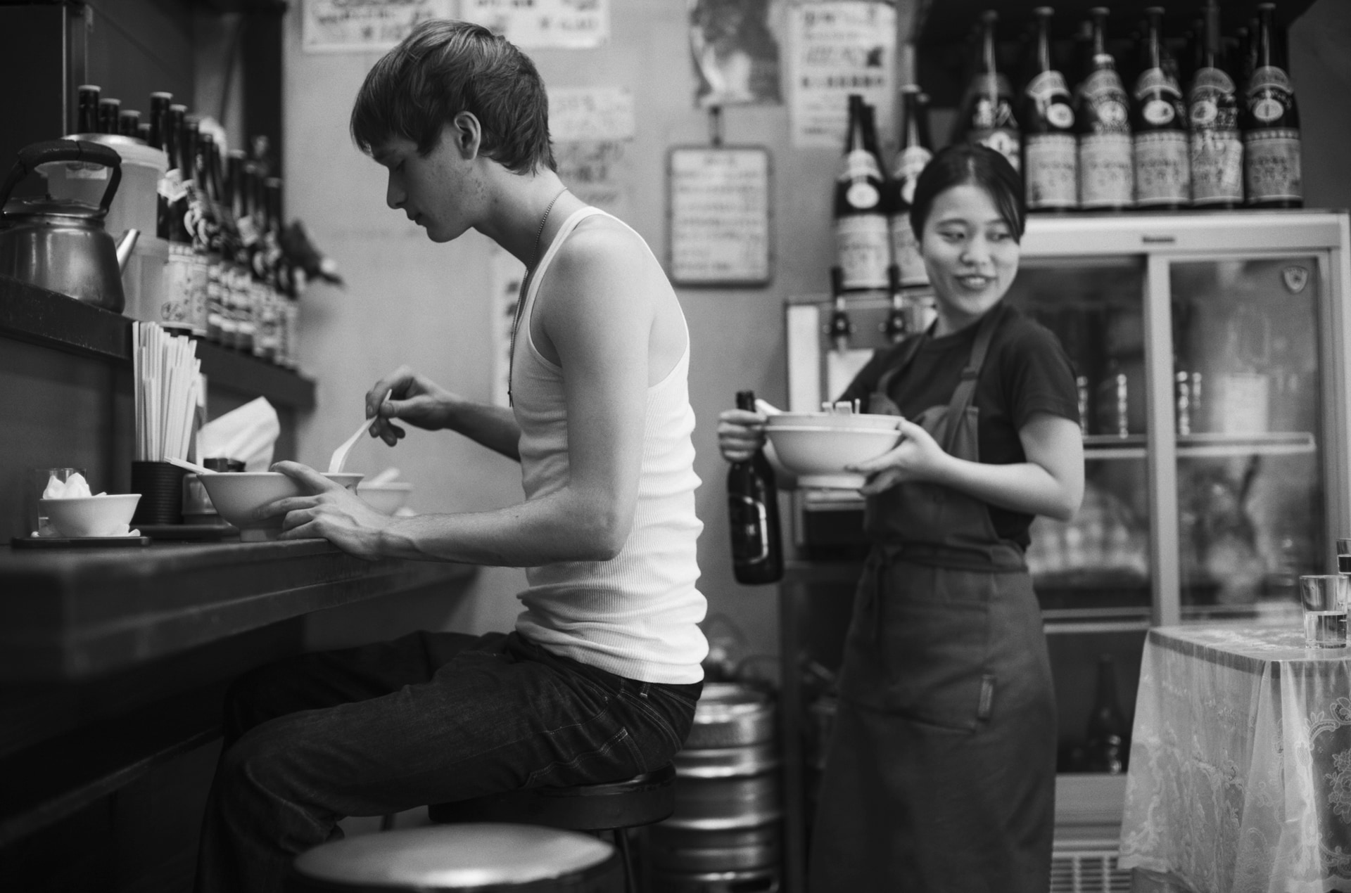 ある夏の日、町中華のカウンターでランニングシャツ姿の男性を見かけ、声をかけてみるとフランスから来たモデルだという。背後ではアルバイトの女性が食器を下げ、ほかのお客さんもいる。そんな飾らない日常の空気感が気に入っている<br><span class="fnt-85">Leica Camera ライカM10モノクローム／ノクティルックスM f0.95/50 ASPH.／50mm／マニュアル露出（F0.95、1/250秒）／ISO 400</span>