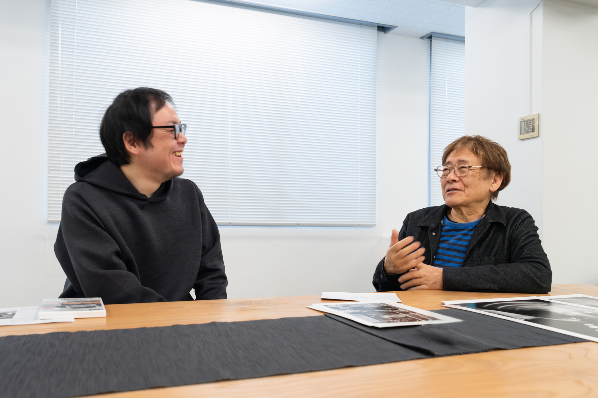 （左）高橋尚紀<br>1988年、東京都出身。日本写真芸術専門学校卒業後、山ノ手写真でインクジェットプリントの出力を担当。プリンティングディレクターとして、さまざまな作家の作品を手掛けている。<br>　<br>（右）ハービー・山口<br>1950年、東京都出身。大学卒業後の1973年にロンドンに渡り10年間を過ごす。帰国後も国内アーティストとのコラボレーションをしながら、市井の人々にカメラを向け続けている。