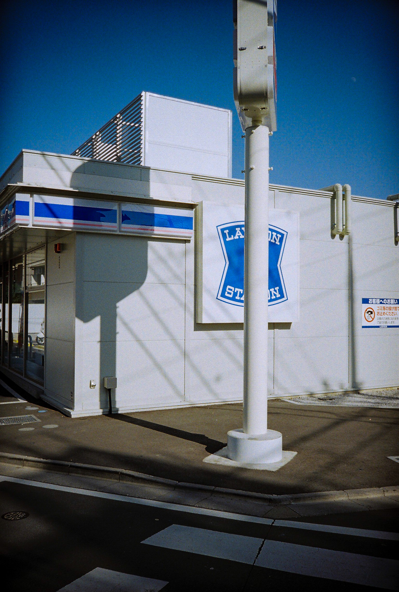 青い空と青い看板と白い壁。きっちりした描写ですが、なぜか周辺光量低下が目立つ謎。かなり絞られているはずですが、現像するまでは結果はわからないし。<br><span class="fnt-85">Lomo MC-A／MINITAR-II 32mm F2.8／プログラムAE／lomography Color Negative 35mm ISO 400</span>