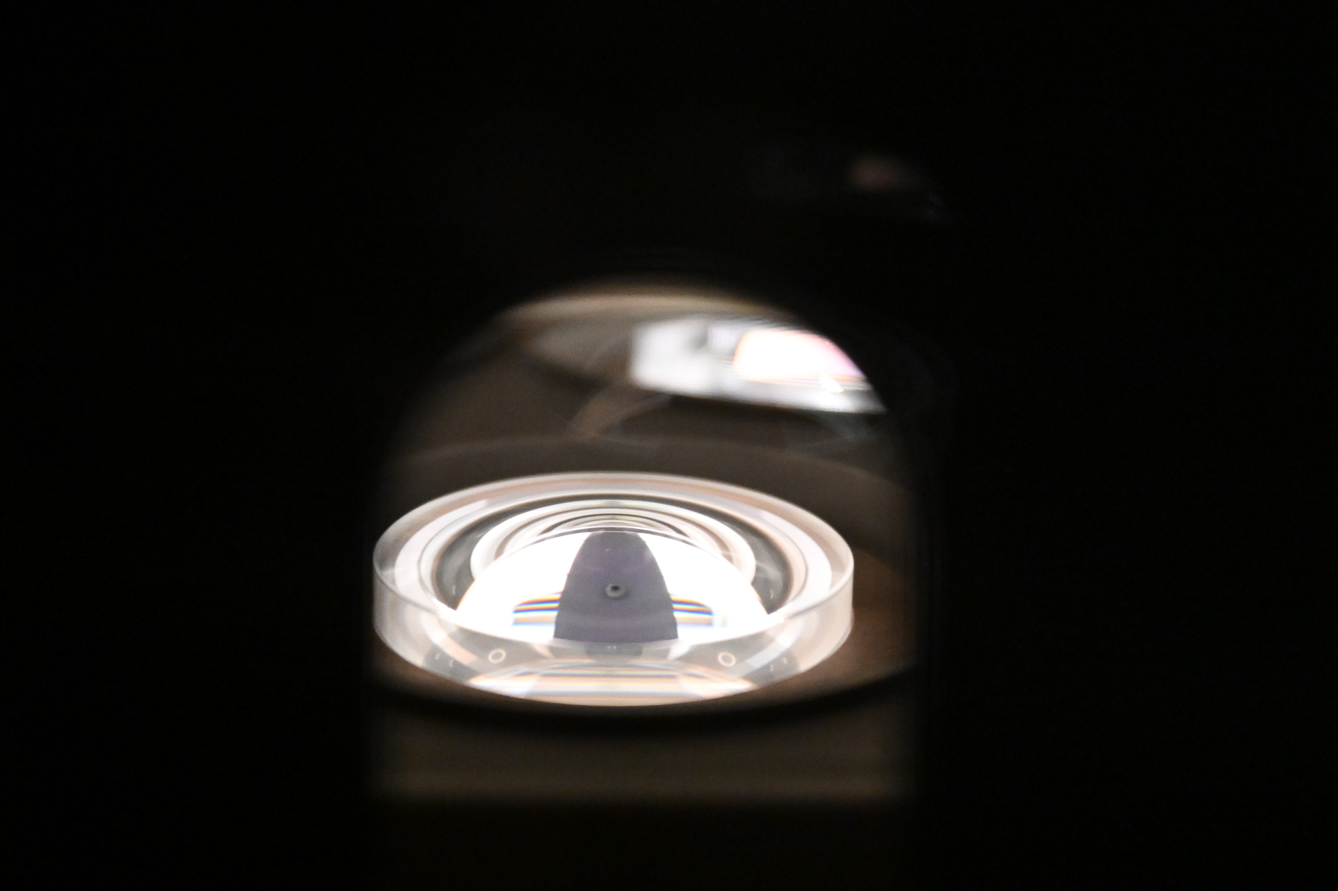 チャンバーの窓にレンズを押し当てて撮影。電子銃でコーティング材料を数千度に加熱・拡散させ、10層ほどのコーティングを形成する。写真で見えているのは上側で、実際にコーティングしているのは下側