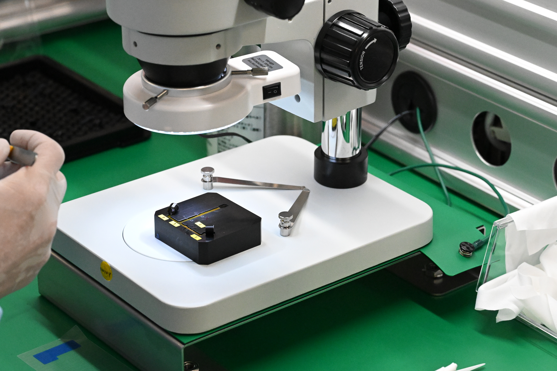 現代レンズには電気部品も欠かせない。ここはFPC（フレキシブルプリント基板）の作業工程。ガイド溝のある治具にFPCのシート部分を置いて固定し、ピンセットでパーツを載せていく