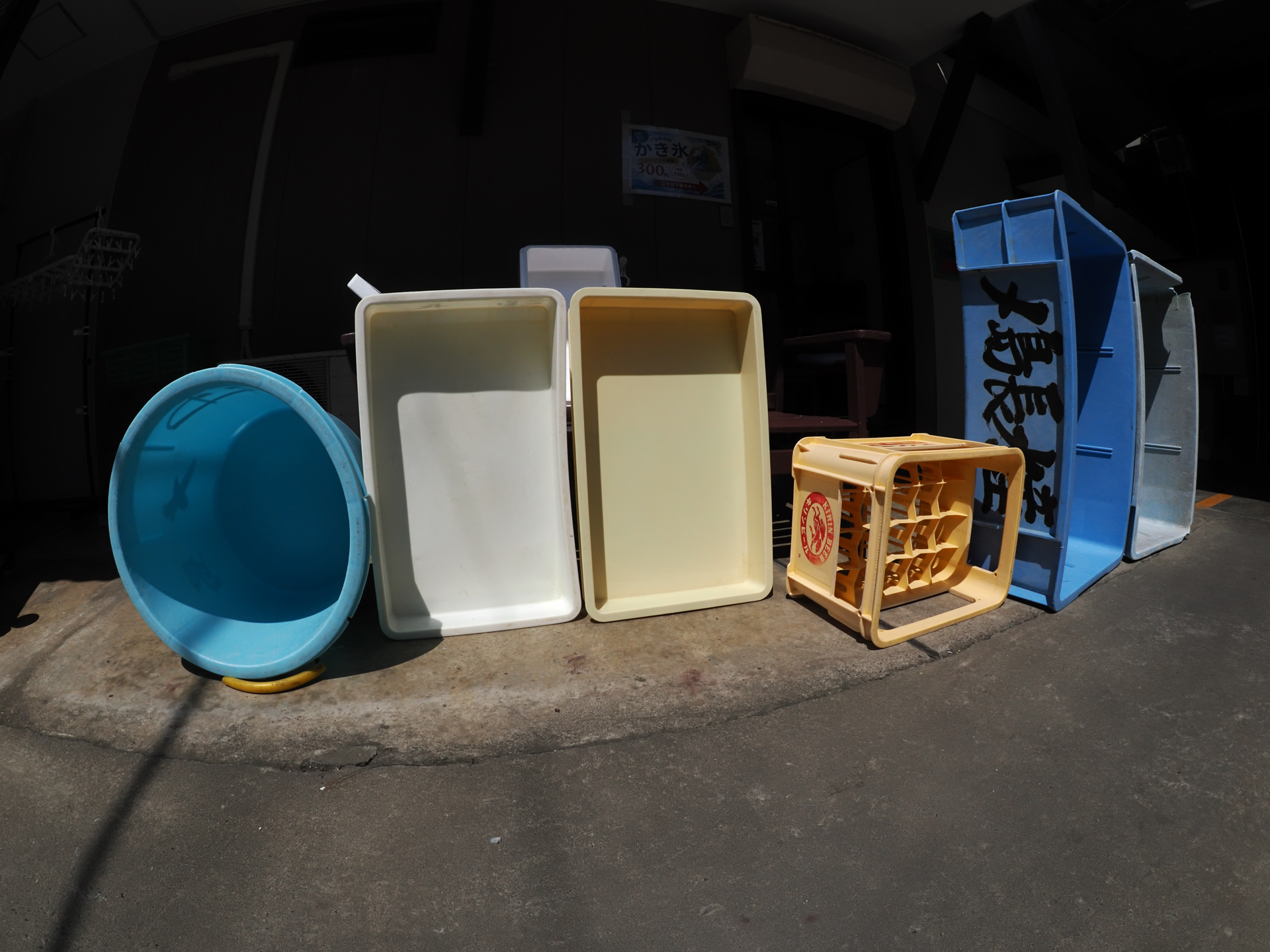 魚屋さんの前に並べられた箱。おじいさんは足が痛いので自分はしゃがむことなく、バリアングルLCDでフレーミングして撮影しております。カメラの位置が偶然よかったのか、魚眼レンズなのに不自然な再現ではないですね。<br><span class="fnt-85">オリンパス OM-1／M.ZUIKO DIGITAL ED 8mm F1.8 Fisheye PRO／8mm／プログラムAE（1/2,000秒、F10、−0.7EV）／ISO 400</span>