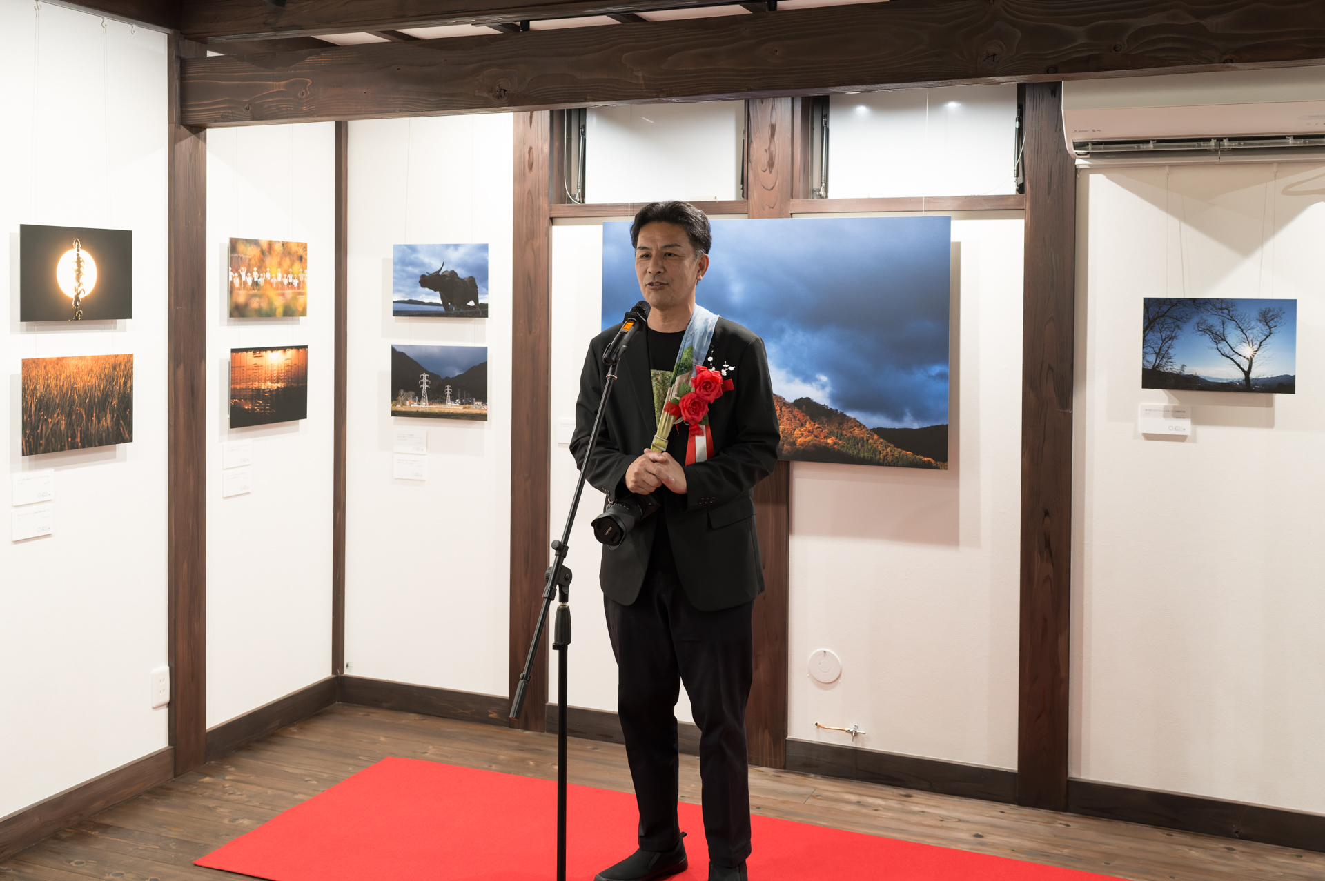 写真家の並木隆氏。背面に並ぶ作品は写真展「ニイハル・クロニクル」。作品販売や写真をもとにしたグッズ展開を通じて、「写真を買う」という文化もこのギャラリーから発信していきたいという
