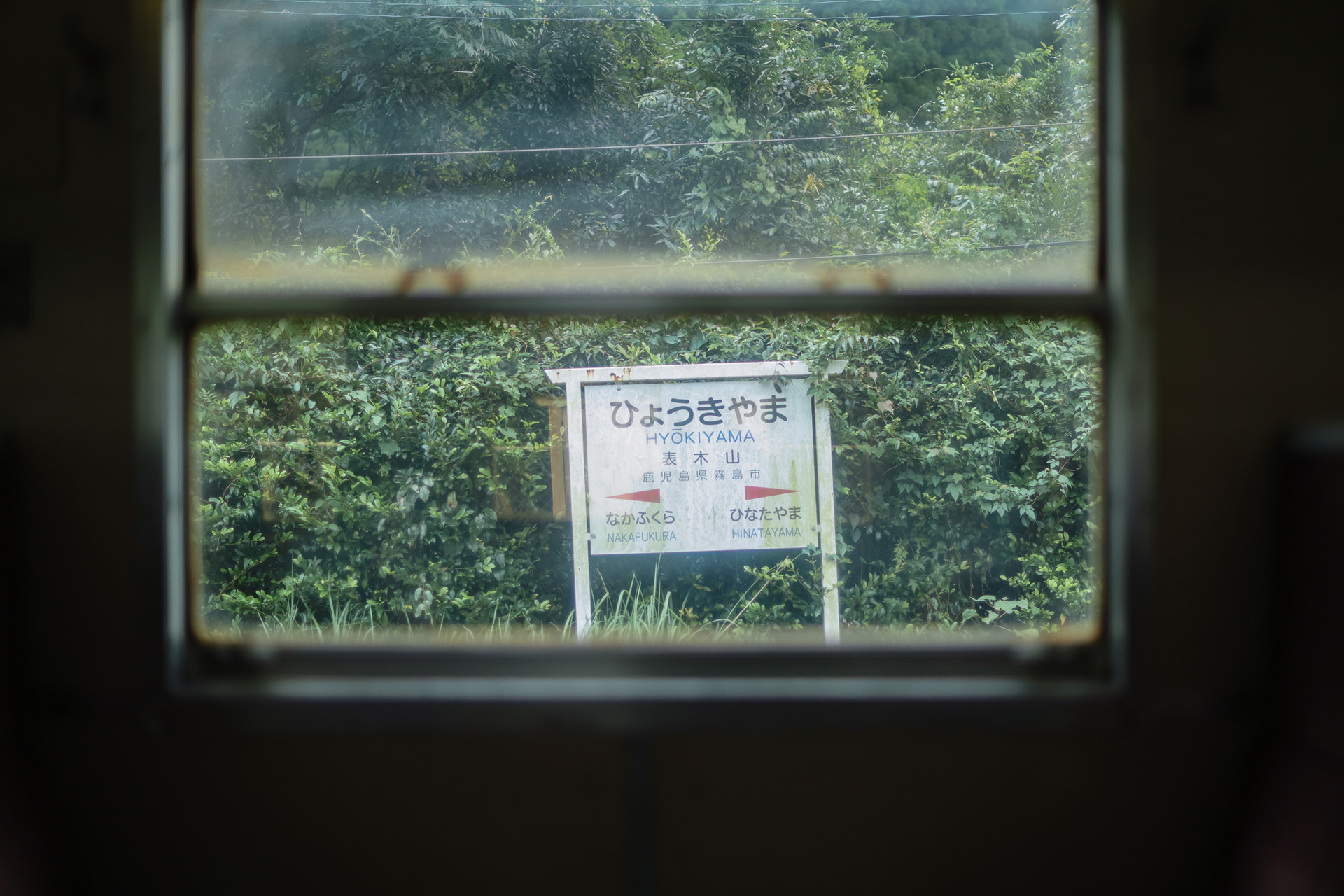 列車が停車すると窓の外に傾いた駅名標が顔を出した。ほほ笑ましい姿に思わずシャッターを切る。NegativeFilmtoneを使って懐かしい雰囲気に仕上げた<br><span class="fnt-85">キヤノン EOS R8 Mark II／RF45mm F1.2 STM／45mm／マニュアル露出（F1.2、1/1,600秒）／ISO 500／WB：オート／JR肥薩線</span>