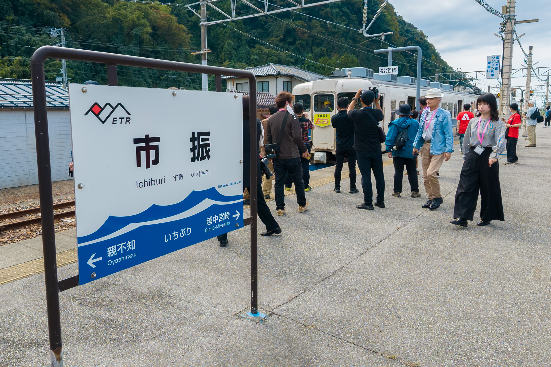 市振駅で過ごす参加者ら。駅名標には日本海をイメージしたイラストが入っている