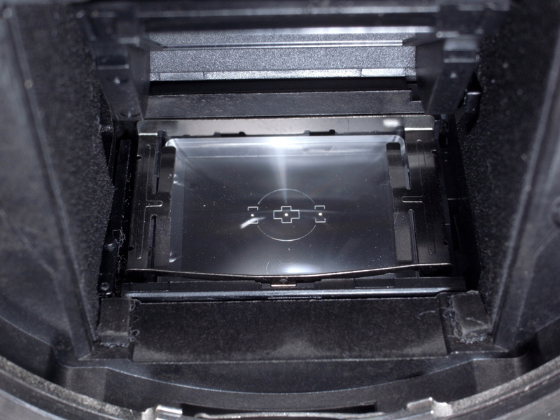 <b>レンズを外したカメラを逆さにし、フォーカシングスクリーンを見るとこんな感じ。フォーカシングスクリーンは、金属製の「押さえ板」（と仮に命名）でミラーボックスに固定されている構造だ</b>