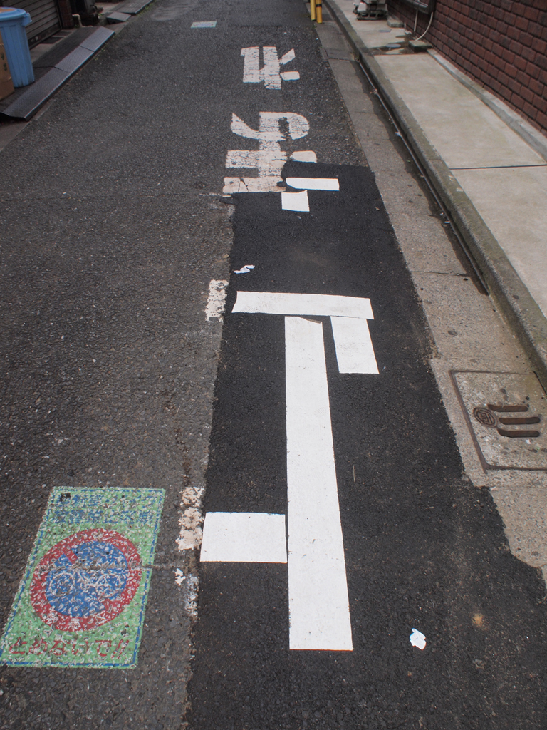 <b>道路工事で欠けてしまった「止まれ」の一部が、書き足されている。乱雑なようでいて、ほんのちょっとだけ残った「止」のオリジナル部分が生かされており、非常なこだわりを感じる</b>