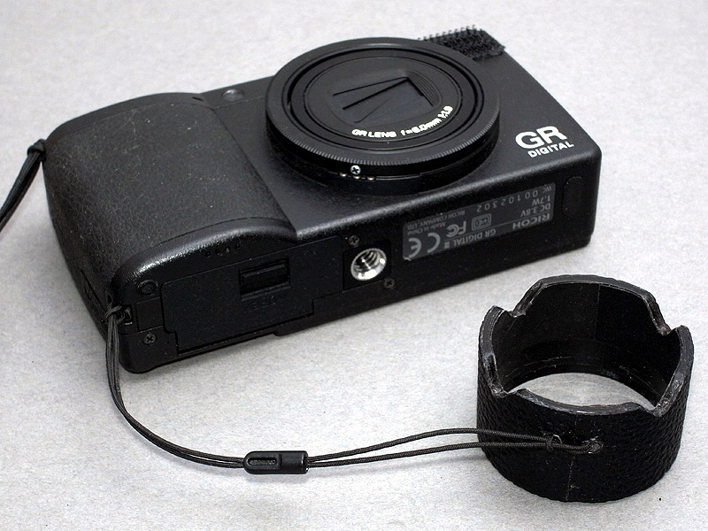 <b>さらにキリで穴を2カ所開け紐を通し、GR DIGITAL IIIのストラップ穴に取り付けると完成。かつてのGR1v用フードは紛失しやすい欠点があったので、その改善策である</b>