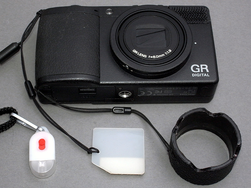 <b>ぼくが愛用しているGR DIGITAL IIIには、現在3つの「外付けアクセサリー」がぶら下がっている。左から夜間照明用ミニLEDライト、以前にも紹介したマクロ用内蔵ストロボディフューザー、そして今回製作したレンズフードである</b>