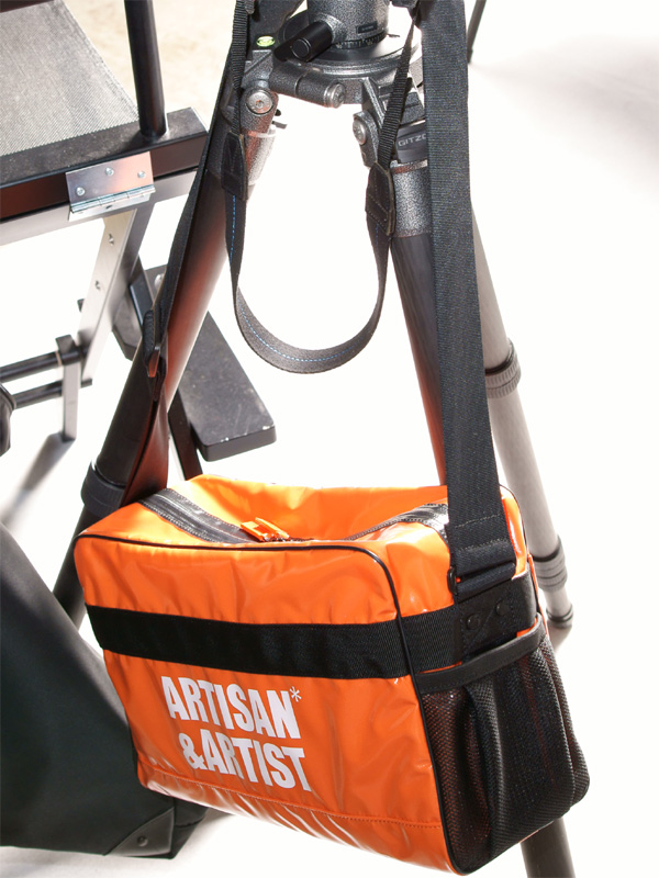 <b>ターポリン素材のバッグを三脚に提げて展示。こちらも名入れおよびデザインが可能という</b>