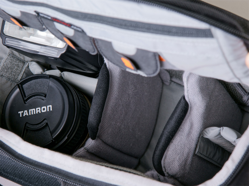 <b>機材を収納。標準ズームレンズを装着したニコンD300と、奥にクリップオンストロボSB-900、ストロボの手前には高倍率ズームレンズを収納している。カメラ本体は黒い縁取りのある仕切りの間に収納</b>