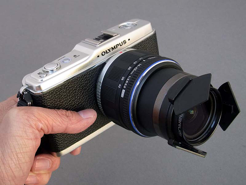 <b>妙な形のレンズフードに見えるが、実はE-P1用標準ズームM.ZUIKO DIGITAL 14-42mm F3.5-5.6に、リコーGX200用の自動開閉キャップ「LC-1」を組み込んでいる。レンズキャップが不要になり、“速写性”が大幅にアップする。例によってぼくのE-P1は、グリップを外して革貼りした改造品である（<a href="http://dc.watch.impress.co.jp/docs/review/labo/20090804_306058.html">こちらの記事を参照</a>）</b>