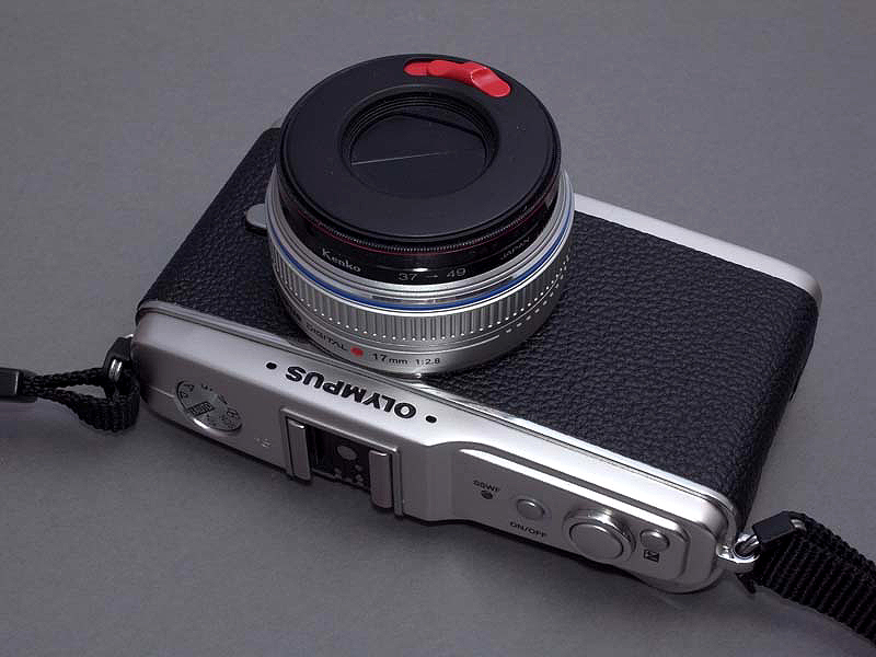 <b>以前の記事で、ぼくが製作したZUIKO DIGITAL 25mm F2.8用の「レンズバリア内蔵キャップ」（<u><a href="http://dc.watch.impress.co.jp/cda/labo/2009/01/26/10058.html">こちらの記事を参照</a></u>）を、E-P1用のM.ZUIKO DIGITAL 18mm F2.8に装着してみた。色がちょっとミスマッチだが（笑）、レンズキャップ着脱の煩わしさが無く、かなり利便性が高い</b>