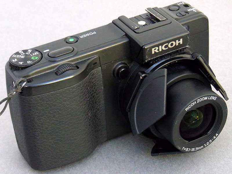 <b>自動開閉キャップLC-1を装着したGX200。電源ONでGX200の沈胴式レンズが伸び、その力でレンズバリアが押し出される。たいへんユニークなアイデアの「外付け式レンズバリア」だが、これを改造し、どうにかM.ZUIKO DIGITAL 14-42mm F3.5-5.6に装着できないかを考えてみた</b>