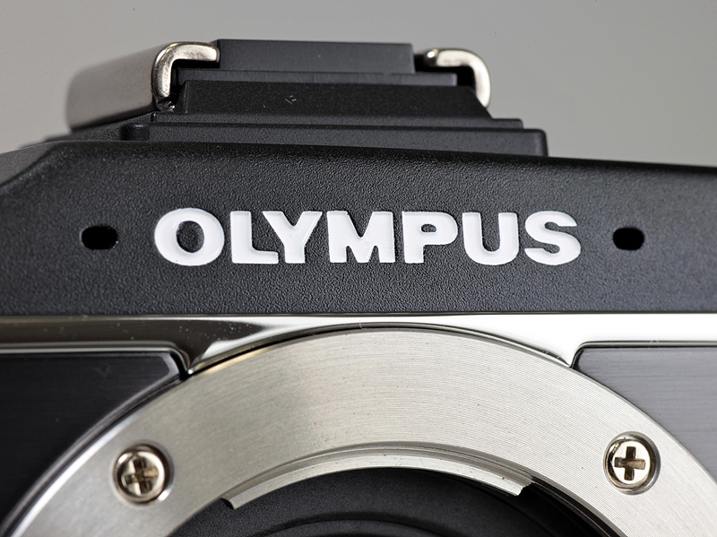 <b>トップカバーはマットな風合いで、OLYMPUSロゴはホワイトになった。ロゴの両脇にステレオマイクを備える。アクセサリーポートの新設により、ホットシュー部分が少し盛り上がった</b>