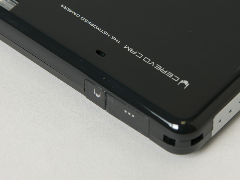 <b>電源のオンオフに使用する「CEREVO」ボタン（左）、レリーズに使用する「…」ボタン（右）。ストラップホールも備える</b>