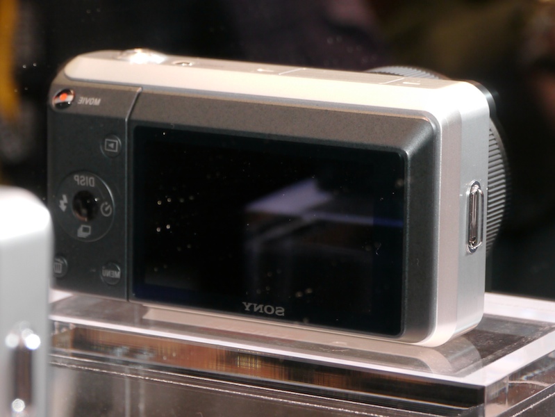 <b>パンケーキスタイルのレンズを装着したシルバーボディのモックアップ。鏡に映った背面には、動画記録用と思われるボタンが見える</b>