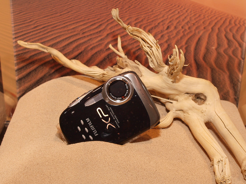 <b>防塵性能を表現したディスプレイ。砂の中にFinePix XP10が埋まっている</b>