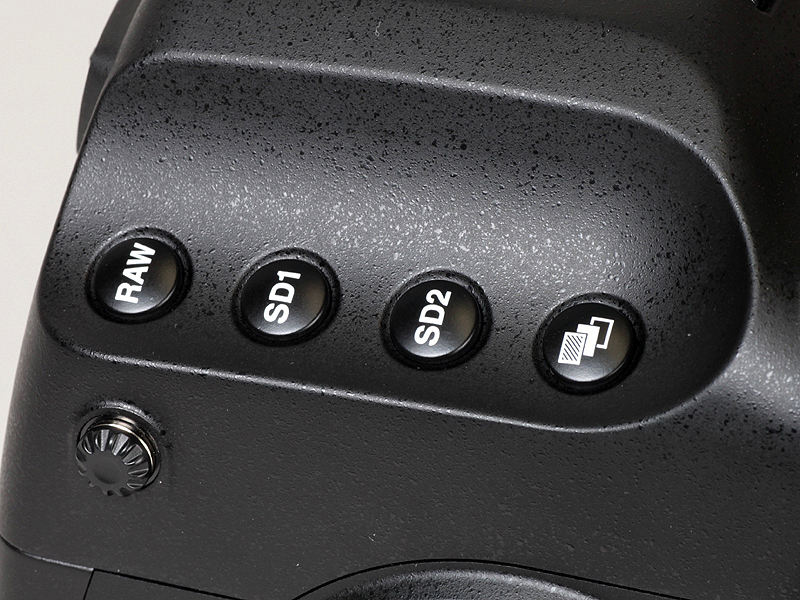 <b>撮影者から見て左側の凹部。中央の2つは、SDスロット1および同2の保存形式設定ボタン</b>