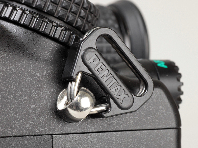 <b>ストラップは三角環による2点吊り。一般的な一眼レフカメラよりも大きめの三角環が付いている</b>