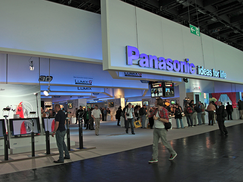 <b>プレスカンファレンスで、DMC-GH2を発表するパナソニックAVCネットワークス社上席副社長の吉田守氏（中央右）とパナソニックAVCネットワークス社DSCビジネスユニット ユニット長の北尾一朗氏（中央左）。右の写真はパナソニックブース正面</b>