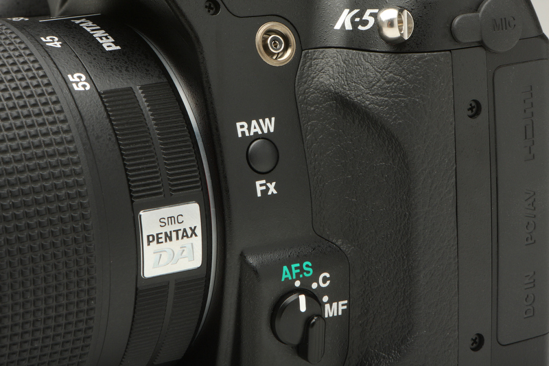 <b>RAWボタンには、露出ブラケット/デジタルプレビュー/電子水準器/構図微調整などの機能を割り当てることができる。シンクロ接点とAFモード切り換えレバーもこの位置に備わる</b>