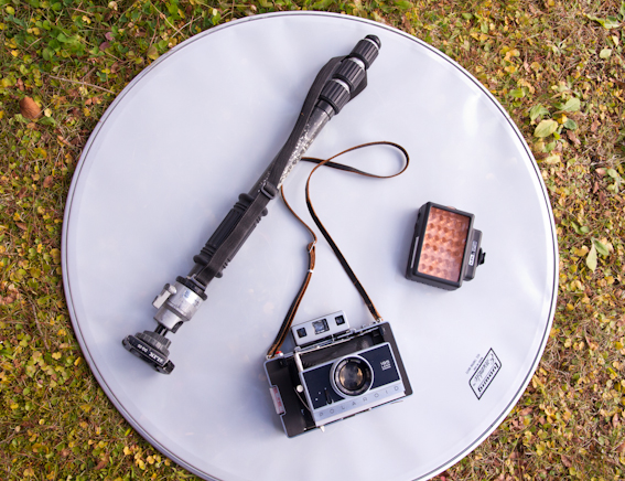 <b>丸レフに見えるのは雑貨屋で見つけたティンパニか何か打楽器のヘッドと呼ばれる部品。中古で1,000円、2枚を即購入して実際に撮影で使っている。手前がポラロイド195ランドカメラ。フィルムは昔はネガ付きのタイプ665というモノクロを使ってたけど、現在は製造してないのでカラーのFP100を使用してスキャニングして原稿としている。右側にあるのはLPL製のLEDライト。被写体が近くて光量がちょっと足りない時などに便利。ムービーにも使えるのでボクも使って重宝しています。スチールと同時にムービーも撮影する横木さんにとっては一脚は必需品。自由雲台にスリックのクイックシューを装着して、これさえあればいつでもどこでも撮影臨戦態勢</b>