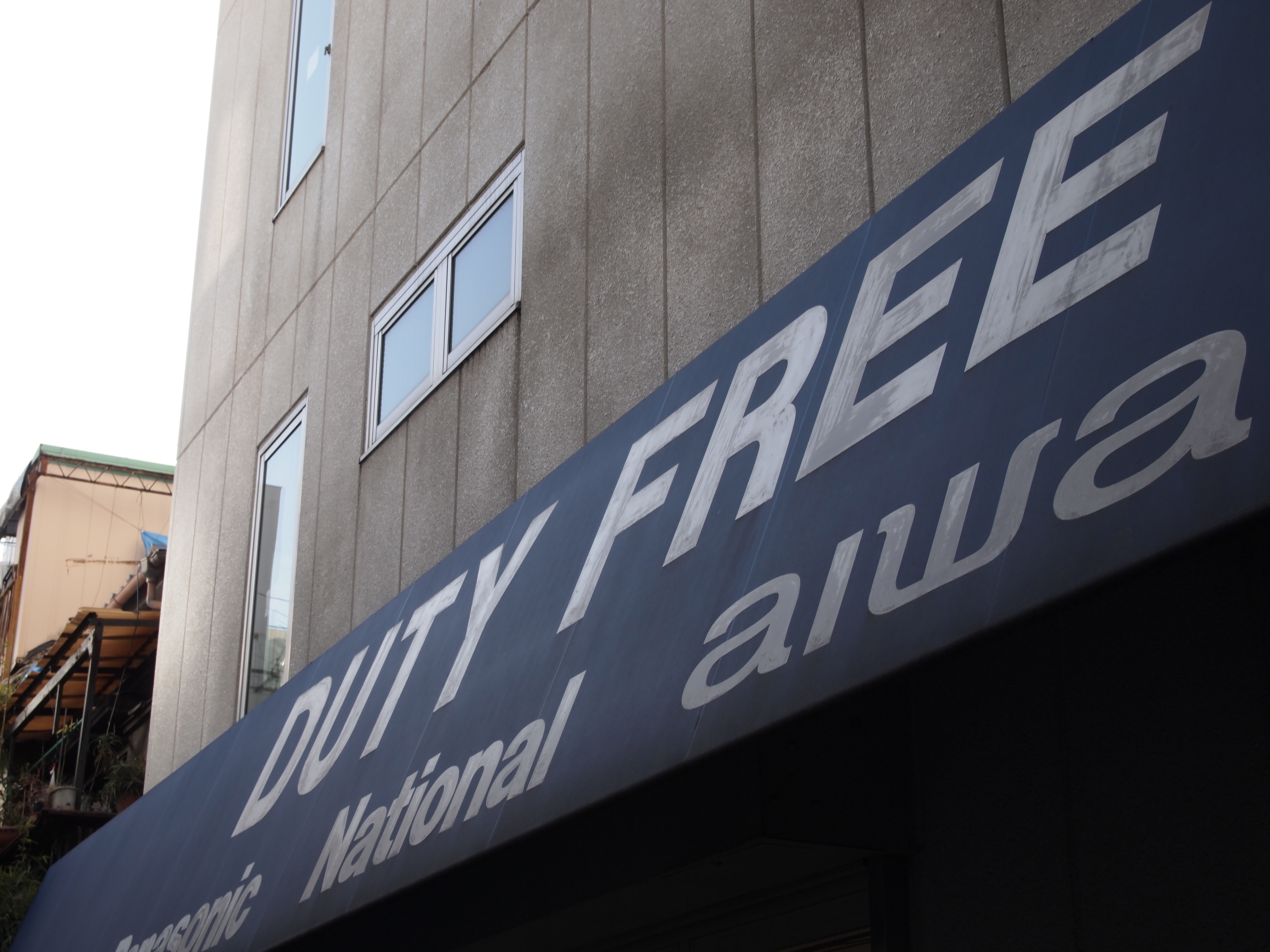 <b>免税品もあつかう電気店。というのは見せかけだけで、窓から見える店内はドラッグストアだったりする<br>E-PL2 / M.ZUIKO DIGITAL 14-42mm F3.5-5.6 II / 4,032×3,024 / 1/125秒 / F8 / 0EV / ISO200 / WB:太陽光 / 27mm</b>