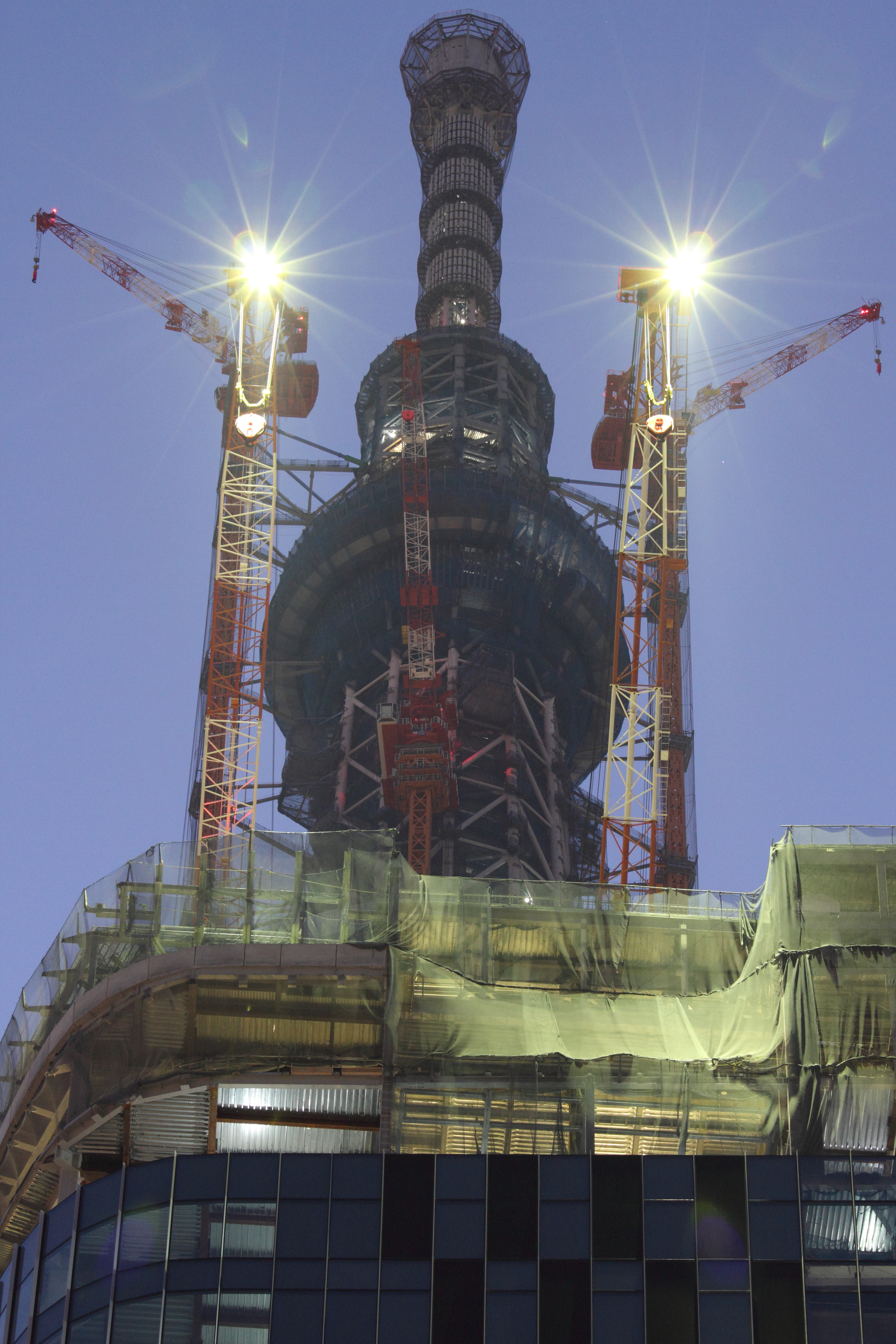 <b>完成後には当然撤去されるクレーンであるが、そのクレーンの1日の作業終了間際に撮影。左右のクレーンがちょうど対称になっているところを狙った。作業ライトは終了後消灯されてしまう。EOS 7D / EF 70-200mm F4 L IS USM / 3,456×5,184 / 1.6秒 / F9 / -0.7EV / ISO1000 / 絞り優先 / WB:オート / 89mm / 17:36</b>