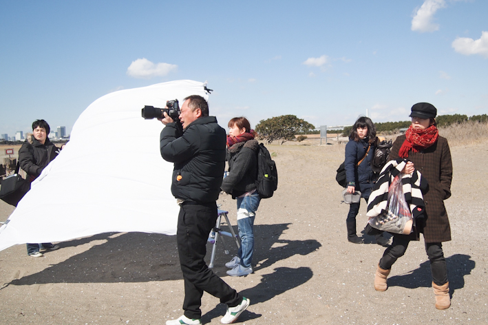 <b>普通のレフ板ではなく、物干し竿のバーを使って大きな白いシーツをクリップで固定して使う。広い面積で柔らかく反射させたり、時にはデュフューザーとしても使えるし、バラしてたためばコンパクトで運べるというマイヤマオリジナル。彼が特許申請をしているかどうかは知らない（笑）</b>