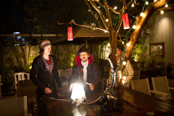 <b>雨が降る中、ライトにカラーフィルターを取り付けたり、飾り付けの明るさを大勢のスタッフで調整してからテスト撮影。春といってもまだ寒いので上着とストーブは必需品なのが屋外撮影の厳しいところ</b>