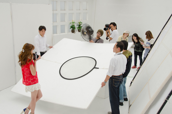 <b>白いスタジオの中に、カポックなどを利用して白いスペースに囲みレフをあてていく。レフの上にさらに丸いレフ板は瞳にうつる反射を考えてのこと。髪の毛を揺らすために、ツッチー自ら扇風機の角度を調整していく</b>