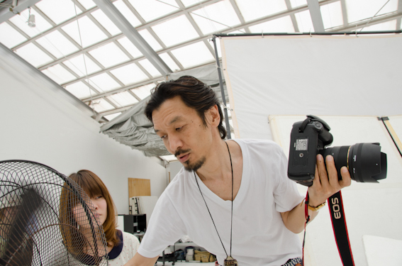 <b>白いスタジオの中に、カポックなどを利用して白いスペースに囲みレフをあてていく。レフの上にさらに丸いレフ板は瞳にうつる反射を考えてのこと。髪の毛を揺らすために、ツッチー自ら扇風機の角度を調整していく</b>