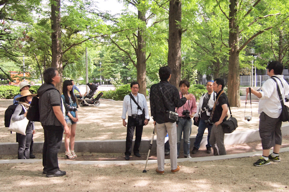 <b>休日に土屋先生の指導ぶりを見学させていただいたのは、彼が担当しているオリンパスズイコ－アカデミーの撮影実習。この日は10名ほどの生徒さんたちが都内の公園に集まっていた。撮影のポイントを説明したら早速みなさんのレンズ群がモデルさんに向けて一斉砲撃を開始したのには驚いた（笑）</b>