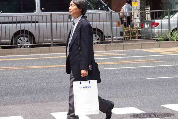 <b>勤務先へは地下鉄で通勤。月曜〜金曜が一般的だが田中さんの部署は行事などによって土日に仕事の場合も少なくない。いつでもバッグには分厚い手帳やパソコンなどがギッシリと詰め込まれていてパンパンに膨らんでいる。そして会社のロゴが入った丈夫な紙袋も資料でいっぱい、肩からはカメラも</b>