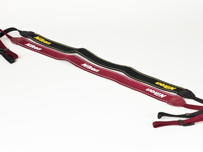 <b>通常のD3100に付属するストラップ（奥）はブラック。レッドのストラップは“Nikon”ロゴが1つ増えた</b>