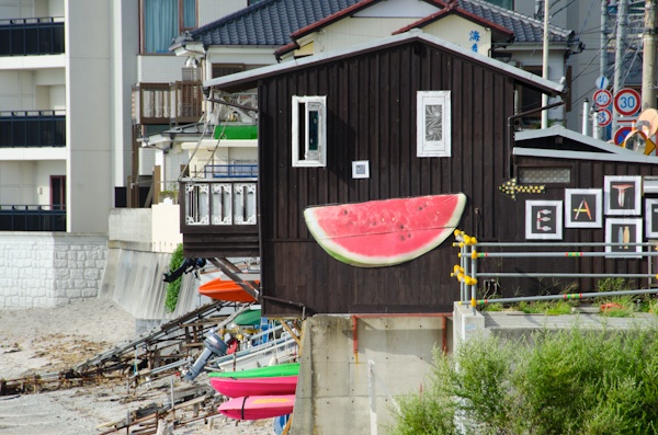 <b>海沿いの道を歩いているとヘンテコリンな建物を見つけた。「へんな建物は何？」って後できいたらココは個人所有の地元の仲間が集まる場所らしく、これもブルースさんが作ったスイカのオブジェだった（笑）。神社にある橋を越えたらオアシスへ到着。現場にはブルースさんの仲間のカメラマンが集まっていた。右写真：左側はミュージシャンを数多く撮っている仁礼博さん、ブルースの右側は日本に於けるサーフィン写真界の第一人者、横山泰介さん。地元の不良オヤジではなくて（失礼！笑）、個性的なおじさんたちだが、そのうちココで登場して頂きたいくらい有名な写真家の先輩たちだ</b>