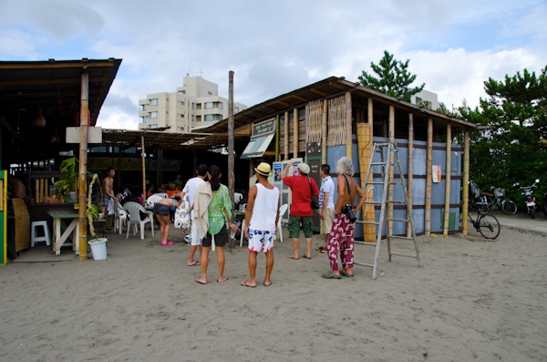<b>海沿いの道を歩いているとヘンテコリンな建物を見つけた。「へんな建物は何？」って後できいたらココは個人所有の地元の仲間が集まる場所らしく、これもブルースさんが作ったスイカのオブジェだった（笑）。神社にある橋を越えたらオアシスへ到着。現場にはブルースさんの仲間のカメラマンが集まっていた。右写真：左側はミュージシャンを数多く撮っている仁礼博さん、ブルースの右側は日本に於けるサーフィン写真界の第一人者、横山泰介さん。地元の不良オヤジではなくて（失礼！笑）、個性的なおじさんたちだが、そのうちココで登場して頂きたいくらい有名な写真家の先輩たちだ</b>