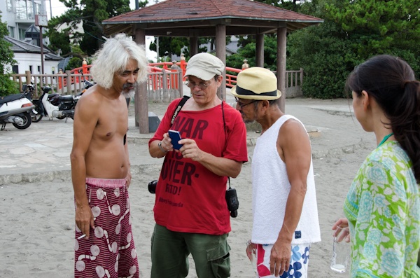 <b>海沿いの道を歩いているとヘンテコリンな建物を見つけた。「へんな建物は何？」って後できいたらココは個人所有の地元の仲間が集まる場所らしく、これもブルースさんが作ったスイカのオブジェだった（笑）。神社にある橋を越えたらオアシスへ到着。現場にはブルースさんの仲間のカメラマンが集まっていた。右写真：左側はミュージシャンを数多く撮っている仁礼博さん、ブルースの右側は日本に於けるサーフィン写真界の第一人者、横山泰介さん。地元の不良オヤジではなくて（失礼！笑）、個性的なおじさんたちだが、そのうちココで登場して頂きたいくらい有名な写真家の先輩たちだ</b>