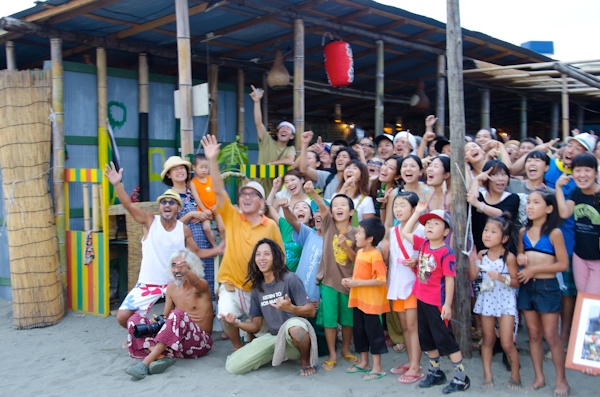 <b>ストロボのヘッドには布袋を被せてデュフューザーとして使う。これがあると無いでは写真の仕上がりの美しさに大きく影響する。そして大きな声でのジョークと合図はカメラマンのお約束の仕事だが、不安定な場所でカメラを構えながらの作業は実は大変なんだ。1、2、3、空が雨雲に変わる前にはみんなの笑顔が撮れて終了、お疲れさまでした。ビールの時間です!</b>