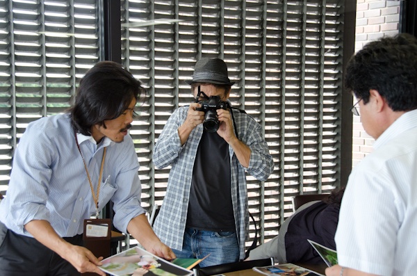 <b>毎日新聞社にて。写真コンテストの審査を務めるブルースさん。会議室に集まったスポンサー各社の担当者さんや主催者、出版社の編集さんなどとともに応募作品から最終選考まで残ったプリントをすべて細かくチェックしていく。最終的に上位受賞作を選ぶという審査も大変だけど重要な仕事のひとつである</b>