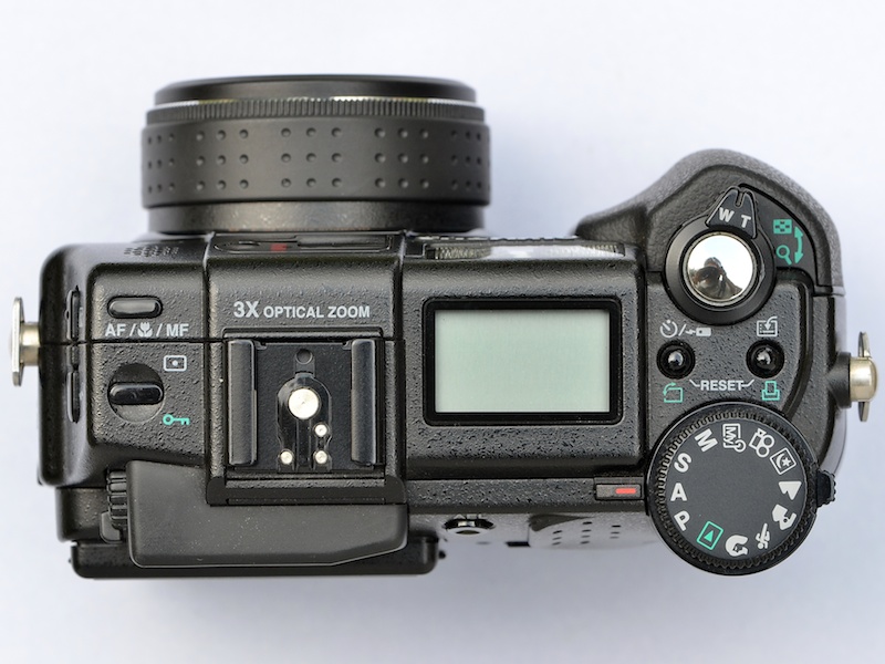 <b>上面部は、グリップとは反対側にはみ出すモードダイヤルが印象的。ファインダー部の出っ張りもカッコイイなぁ〜。反対側の底部は、四隅と三脚穴まわりに埋め込まれたラバー製のパーツが目につく。これによって、接地面との密着度が高まる</b>