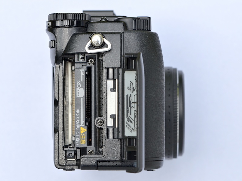 <b>グリップ部の横のカードカバーを開くと、メディアスロットが2つ並ぶ。撮影者手前側がCFスロットで、レンズ側がxD・SMスロット</b>