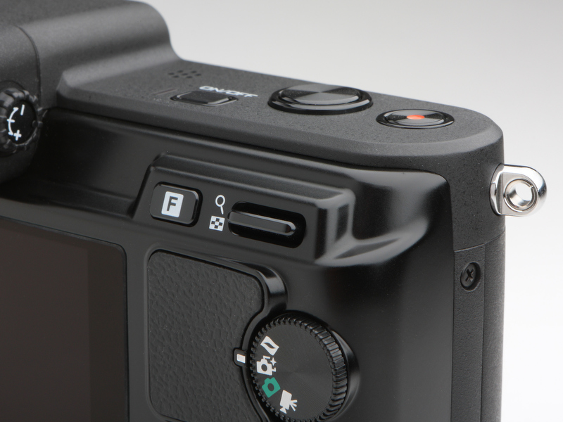 <b>目新しいフィーチャーボタンとサムネイル/拡大レバー。フィーチャーボタンは、静止画撮影モード時にはシャッターの選択（メカニカル/エレクトロニック/エレクトロニックHi）が行なえる。撮影モードダイヤルに搭載されるモードは、コンパクトデジカメ並みにシンプル</b>