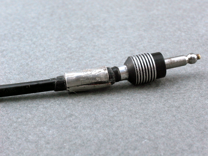 <b>連動ケーブルのミラーハウジング差し込み口。ケーブルのボタン押すと先端のピンが引っ込み、セットしたミラーがアップする仕組みになっている。実はこのケーブル、買ったときに外側のビニールが一部切れていて、中のワイヤーが剥き出しになっていた。なのでその部分をアルミ板で巻きレストアをしている。さらに補強と保護のため、この上に製本テープを巻いている</b>