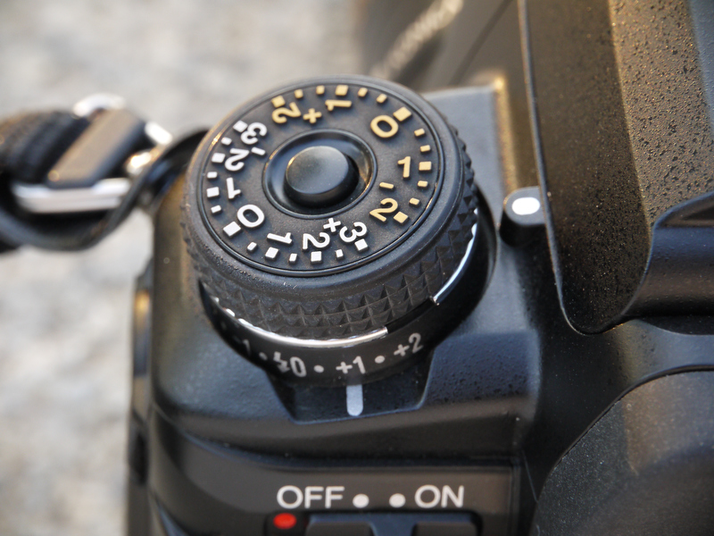 <b>右手側の「露出モードダイヤル」の基部には「ドライブモードレバー」があり、左手側の「露出補正ダイヤル」の基部には「ストロボ調光補正レバー」がある。ちなみに、両ダイヤルにはロック機構があるが、両レバーにはロック機構はない</b>