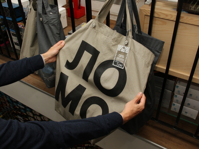 <b>同店でカメラ以外の人気商品というバッグ。写真のモデルはロシア文字の「ロモ」をあしらっている。大きな荷物を持ち歩く専門学校生などが買っていくそうだ。店内にはバッグ以外のアパレルグッズも並んでいた</b>