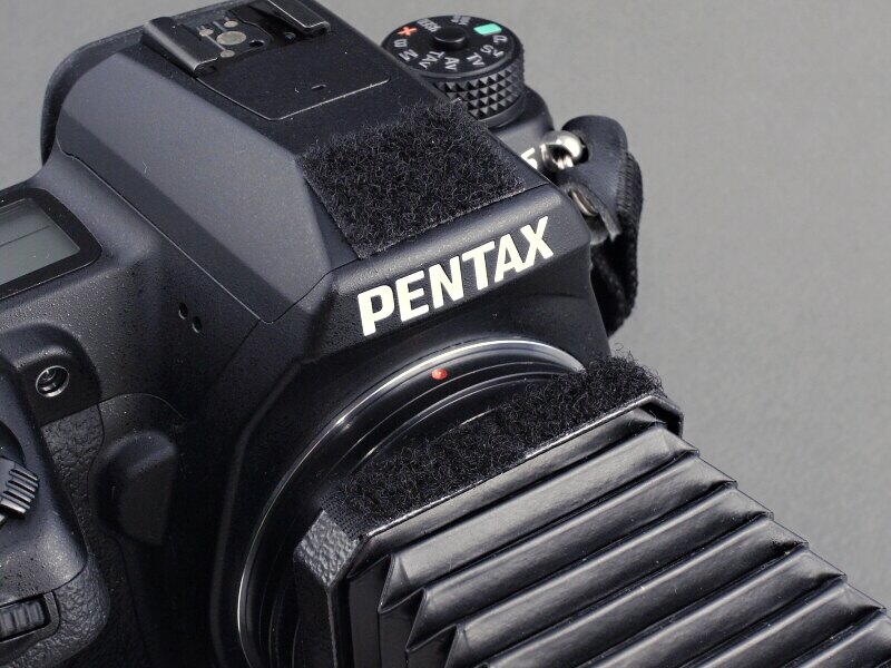 <b>さらにベローズを実用的に使用する工夫を行なう。軽快な自動絞りの機構を活かして“手持ち撮影仕様”に仕立てる方針だ。まずはカメラのストロボカバーとベローズ基部にマジックテープを貼る</b>